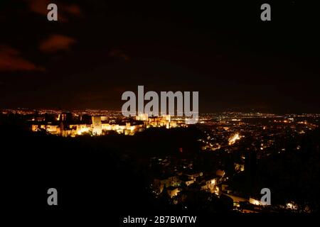 Blick auf die Alhambra in Granada, Spanien. Das Gebäude ist beleuchtet und es sind Lichter aus der umliegenden Stadt zu sehen. Stockfoto