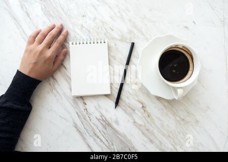 Draufsicht Bild einer Hand, die sich auf ein leeres weißes Notizbuch mit Kaffeetasse auf dem Tisch aufschreiben wird Stockfoto