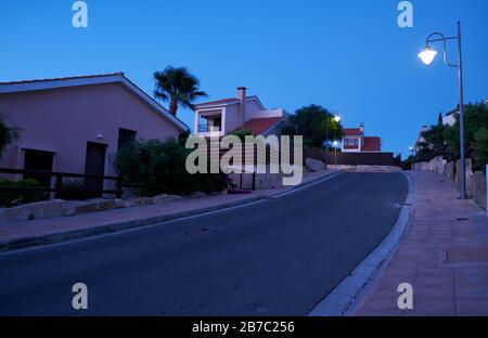 Der Blick auf die Straße mit der Linie der Wohnhäuser des Dorfes Pissouri im Abendlicht. Bezirk Limassol. Zypern Stockfoto