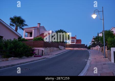 Der Blick auf die Straße mit der Linie der Wohnhäuser des Dorfes Pissouri im Abendlicht. Bezirk Limassol. Zypern Stockfoto