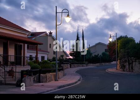 Der Blick auf die Straße mit der Linie der Wohnhäuser des Dorfes Pissouri im Abendlicht. Bezirk Limassol. Zypern Stockfoto