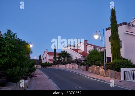 Der Blick auf die Straße mit der Linie der Wohnhäuser des Dorfes Pissouri im Abendlicht. Bezirk Limassol. Zypern Stockfoto