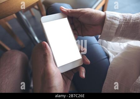 Verspottes Bild der Hände von Mann und Frau, die ein weißes Mobiltelefon mit leerem Desktop-Bildschirm zusammen halten und betrachten Stockfoto
