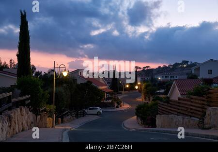 Der Blick auf die Straße mit der Linie der Wohnhäuser des Dorfes Pissouri im Abendlicht. Bezirk Limassol. Zypern Stockfoto