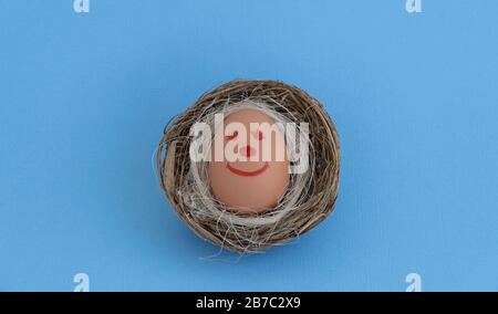 Fröhliches Osterei. Lustige Smiley-Gesichter auf einem Ei. Nisten Sie auf blauem Hintergrund. Osterei mit niedlichem, handgezeichnetes Gesicht. Stockfoto