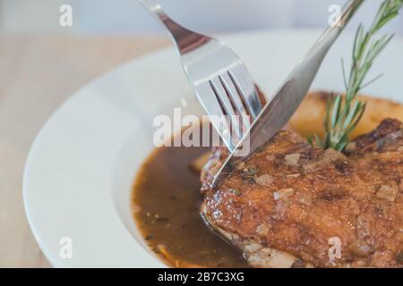 Nahaufnahme von Menschen, die mit Messer und Gabel Hühnereintopf auf Holztisch essen Stockfoto