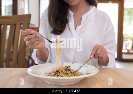 Nahaufnahme einer Frau, die würzige Speckspaghetti auf Holztisch isst Stockfoto