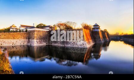 Wassergraben um Steinmauern von historischem Palast, Park und Schloss in Osaka Stadt Japan. Weich aufsteigende Sonne über Horizont. Stockfoto