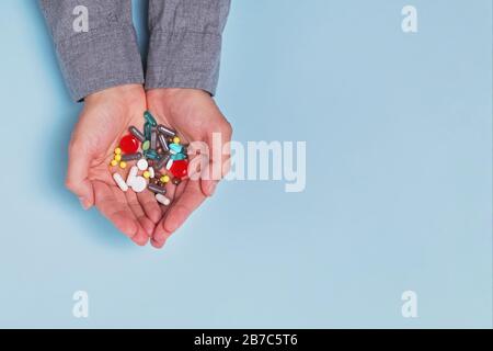 Die Hände des Mannes halten viele verschiedene Tabletten und Pillen in seinen Händen über blauem Hintergrund Stockfoto