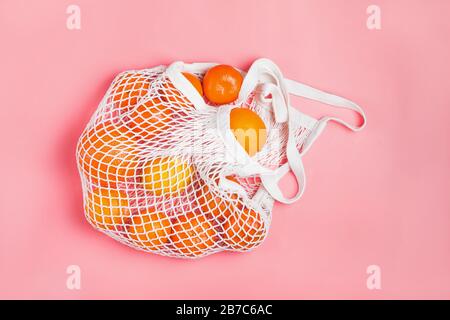 Einkaufstasche aus Mesh mit Zitronen und Orangen auf pinkfarbenem Hintergrund. Stockfoto