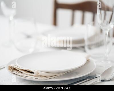 Schöne Tischeinstellung in weißen Farben. Leere weiße Platten. Tisch für ein romantisches Abendessen für zwei Personen zu Hause Stockfoto