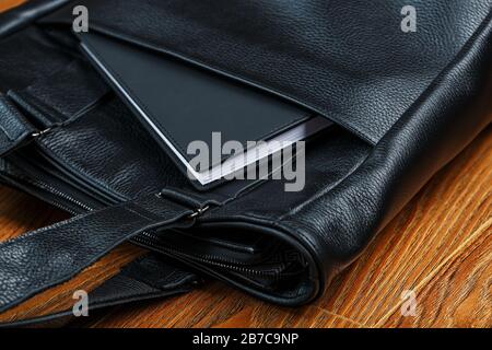 Schwarzes Notizbuch, das aus der Tasche einer schwarzen Ledertasche besteht, Nahaufnahme, handgefertigte, natürliche Materialien. Stockfoto