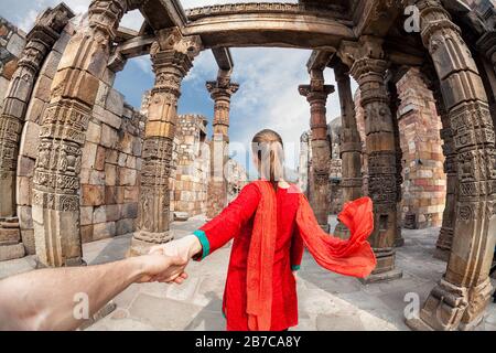 Frau in rotem Kostüm mit Schal, der Mann von Hand zum Qutub Minar Turm in Delhi, Indien führt Stockfoto