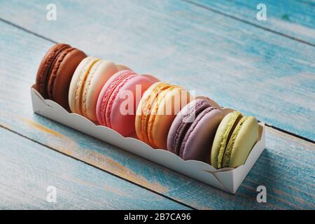 Makkaroni-Kekse in verschiedenen Farben in einer Schachtel auf blauem, altem Holzhintergrund in blauer Farbe. Stockfoto
