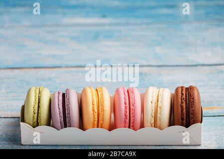 Makkaroni-Kekse in verschiedenen Farben in einer Schachtel auf blauem, altem Holzhintergrund in blauer Farbe. Stockfoto