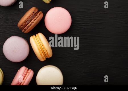 Makkaroni-Kekse in verschiedenen Farben liegen auf einem schwarzen, strukturierten Hintergrund. Freier Speicherplatz. Stillleben von Süßwaren. Stockfoto
