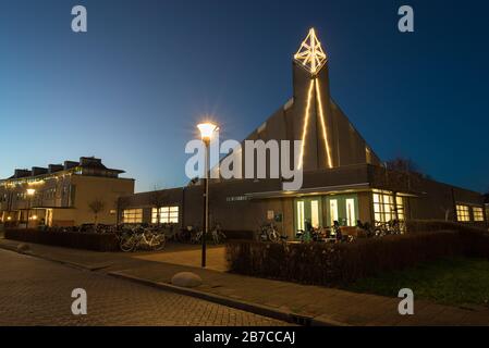 Moderne evangelische Kirche mit Kirchturm wird nach Sonnenuntergang beleuchtet. Der Name der Kirche ist 'Morgenster' (Morgenstern), geschrieben an der Kirchenwand. Stockfoto