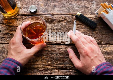 Mann, der ein Glas Whisky hält und eine Zigarette raucht Stockfoto