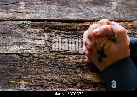 Der Mann betete mit einem Kreuz in den Händen auf dem Holzhintergrund mit Platz für Text Stockfoto