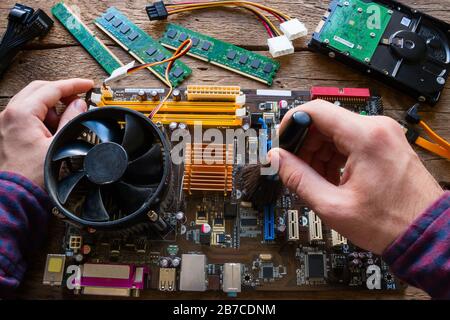 Man reinigt den Staub von der Hauptplatine des Computers auf einem Holzhintergrund Stockfoto