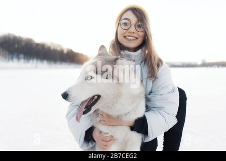 Glückliche junge Mädchen spielen mit sibirischen Husky Hund in Winter Park. Sie gehen auf einem zugefrorenen See Stockfoto