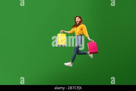 "Excited Girl Running Holding Shopper Bags On Green Background" Stockfoto