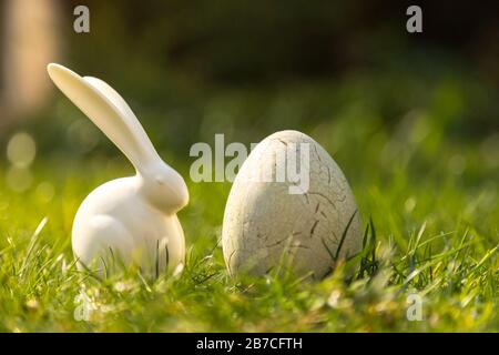 Weiße Osterhasen-Figuren und gefärbte Eier auf dem Grün Gras auf dem Feld an einem sonnigen Tag Stockfoto