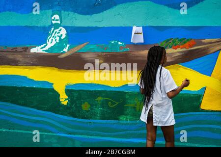 Eine afro-kolumbianische Studentin malt ein gesellschaftliches und umweltbezogenes Wandbild an einer Schulwand in Quibdó, Kolumbien. Stockfoto