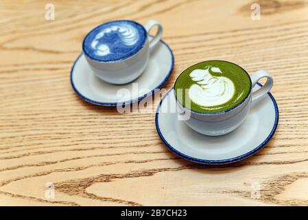 Matcha, grüner und blauer Teelatte in zwei Tassen. Brauner Holzhintergrund. Draufsicht. Stockfoto