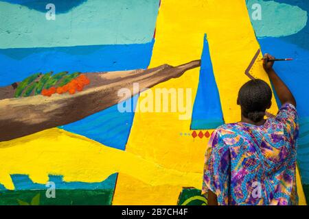 Eine afro-kolumbianische Studentin malt ein gesellschaftliches und umweltbezogenes Wandbild an einer Schulwand in Quibdó, Kolumbien. Stockfoto