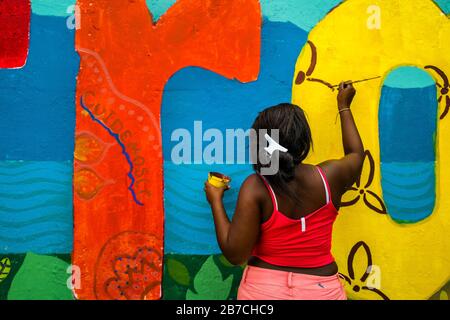 Eine afro-kolumbianische Studentin malt ein gesellschaftliches und umweltbezogenes Wandbild an einer Schulwand in Quibdó, Kolumbien. Stockfoto