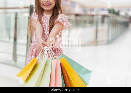 Ein kleines Mädchen hält mehrfarbige Pastelltaschen in den Händen. Das Konzept des Einkaufs, des Einkaufs im Einkaufszentrum. Nahaufnahme. Stockfoto