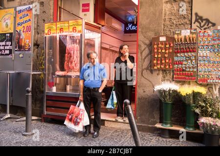 Ein älteres Paar pausiert vor einer Metzgerei in einer Straße von Neapel, Italien. Stockfoto