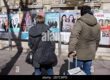 Lyon, Frankreich. März 2020. Die Wähler in Lyon, Frankreich, außerhalb eines Wahllokals, sehen in der heutigen ersten Runde der lokalen Wählerschaft Plakate für Kandidaten an. Credit: James Colburn/ZUMA Wire/Alamy Live News Stockfoto