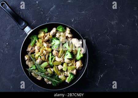 Fitness-Menü: Sauiertes Hühnerfleisch mit grünem Gemüse: Zucchini, Brokkoli, Zwiebel und Rosmarin auf einem Skillet auf dunklem Betongrund, flacher Lay Stockfoto