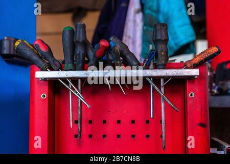 Schraubendreher und Schraubenschlüssel am Arbeitsplatz einer Autowerkstatt auf einem roten Schreibtisch mit Regalen 2020 Stockfoto