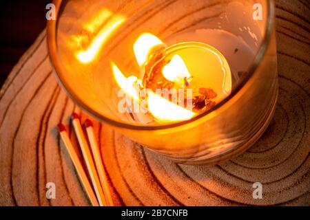 Schwere brennende Kerze in einer Galss auf einer Holzplattform mit Streichhölzern daneben, Flammen, Feuer, Holz Stockfoto