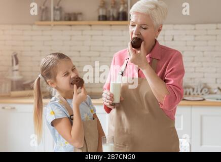 Oma und Enkelin essen leckere Schokoladenmuffins in der Küche Stockfoto