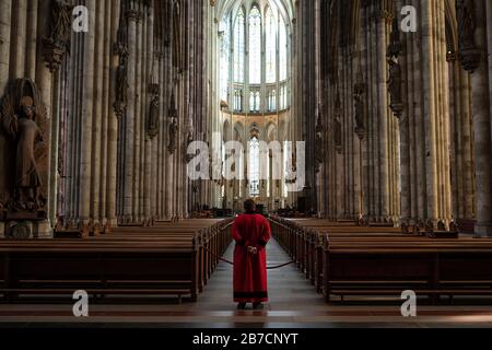 Köln, Deutschland. März 2020. Ein Domschweizer steht im leeren Kölner Dom zwischen den Bänken. Der Dom ist ab Sonntag nur noch für Menschen geöffnet, die ihn zum Beten besuchen wollen. Gottesdienste werden in der Kamera gefeiert und von Domradio.de ausgestrahlt. Achtung: Nur im Zusammenhang mit der Berichterstattung über die Maßnahmen des Kölner Doms in der aktuellen Corona-Epidemie verwenden. Credit: Marius Becker / dpa / Alamy Live News Stockfoto