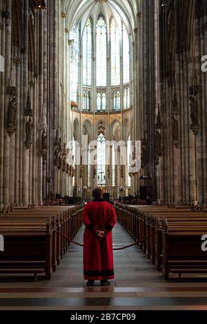 Köln, Deutschland. März 2020. Ein Domschweizer steht im leeren Kölner Dom zwischen den Bänken. Der Dom ist ab Sonntag nur noch für Menschen geöffnet, die ihn zum Beten besuchen wollen. Gottesdienste werden in der Kamera gefeiert und von Domradio.de ausgestrahlt. Achtung: Nur im Zusammenhang mit der Berichterstattung über die Maßnahmen des Kölner Doms in der aktuellen Corona-Epidemie verwenden. Credit: Marius Becker / dpa / Alamy Live News Stockfoto