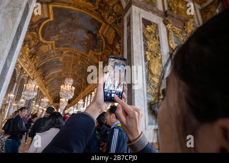 Tourist, der ein Handy-Bild von der Decke des Spiegelsaals im Schloss Versailles am Stadtrand von Paris, Frankreich, Europa, aufgenommen hat Stockfoto