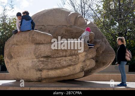 Kinder, die auf einem riesigen Steinkopf spielen, mit gekuppelter Handskulptur "Écoute" des französischen Künstlers Henri de Miller in Paris, Frankreich, Europa Stockfoto