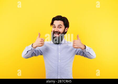 Glücklicher bärtiger Mann, der den Daumen nach oben zeigt und über gelbem Hintergrund lächelt Stockfoto