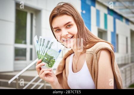 Unbeschwerte junge Frau zeigt Geldstapel von Euro-Banknoten und lächelt glücklich. Erfolgskonzept Business, Income. Stockfoto