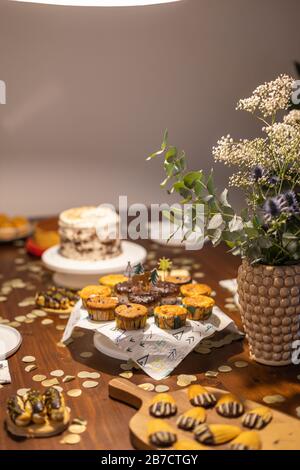 Dekorierter Geburtstagstisch mit verschiedenen Cupcakes, Muffins, Kuchen und Madeleinen mit Blumen und Konfetti. Stockfoto