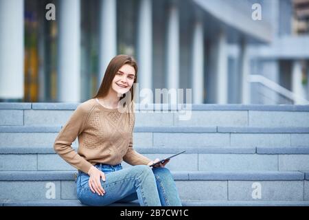 Junges Mädchen, das auf den Stufen sitzt und in die Tablette schaut Stockfoto