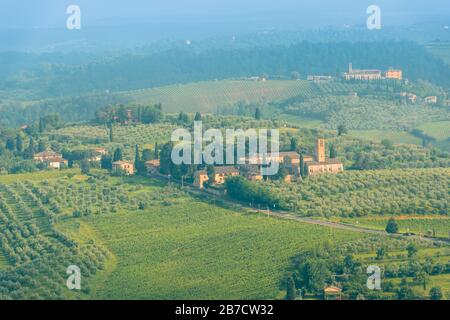 Toskanische Landschaft mit sanften Hügeln, Weinbergen und Bauernhäusern und Santa Maria Assunta a Monte Oliveto Minore aus San Gimignano, Toskana, Italien Stockfoto