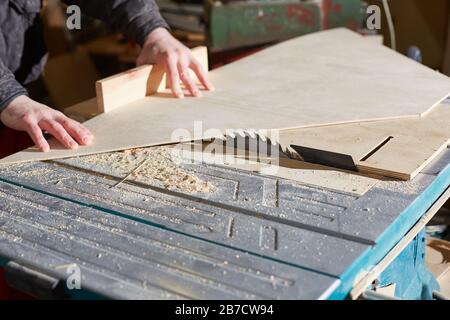 Die Hände eines Arbeiters haben Sperrholz auf einer Maschine mit einer Kreissäge geschnitten. Stockfoto