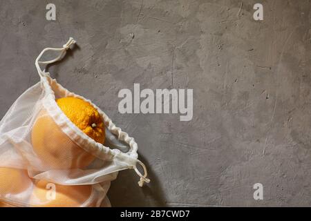 Frucht-Orangen in einem Eco-Beutel mit weißem Netz auf grauem Hintergrund. Copyspace. Stockfoto