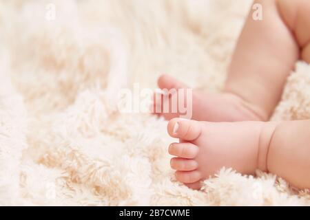 Grußkarte oder Einladung zur Babydusche. Nahaufnahme der Füße des Babys auf einer beigefarbenen, strukturierten Plaid. Copyspace. Glückliches Familien- und Mutterschaftskonzept. Stockfoto